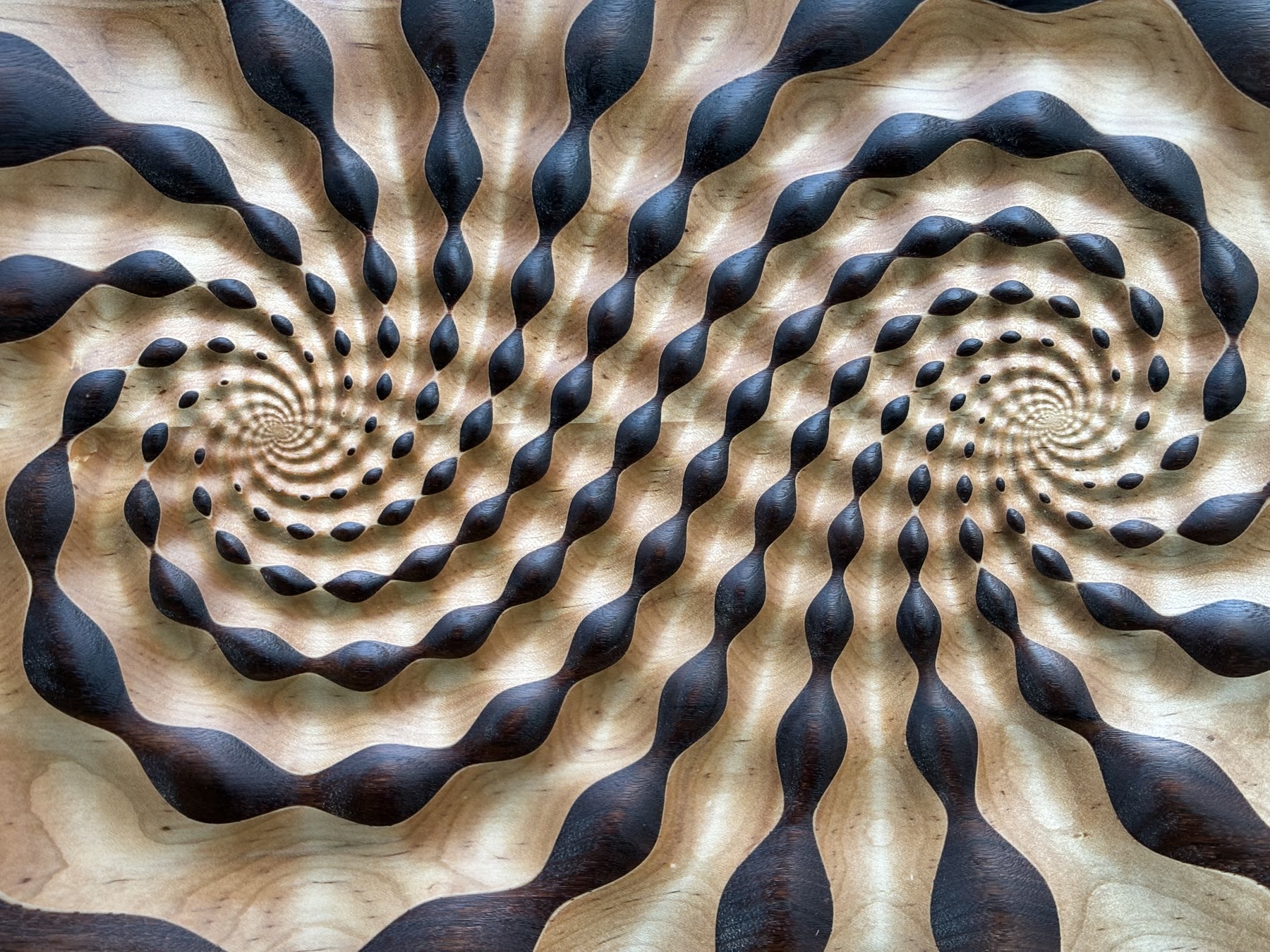 Straight-on close view of the finished panel, showing walnut and maple curves winding into the two spiral centers.